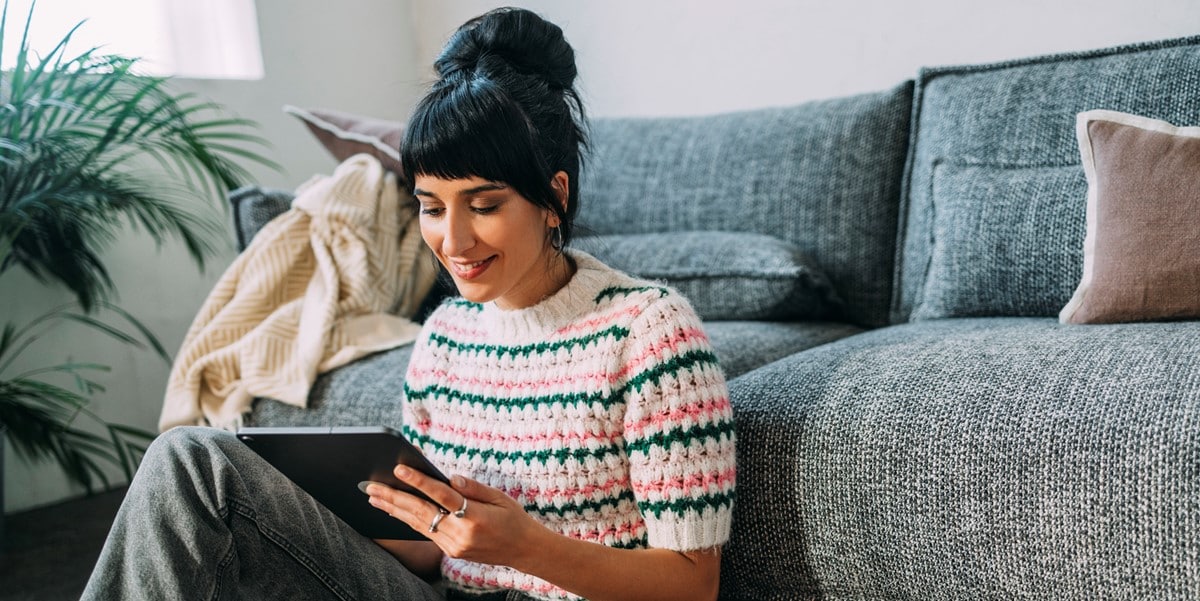 woman sitting in front of couch, looking at tablet